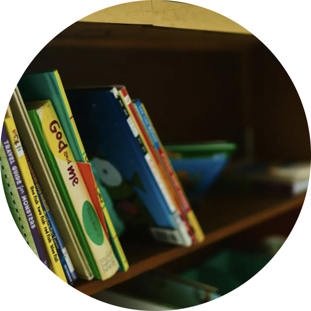 A row of children’s books standing upright on a wooden bookshelf, with some book titles partially visible.
